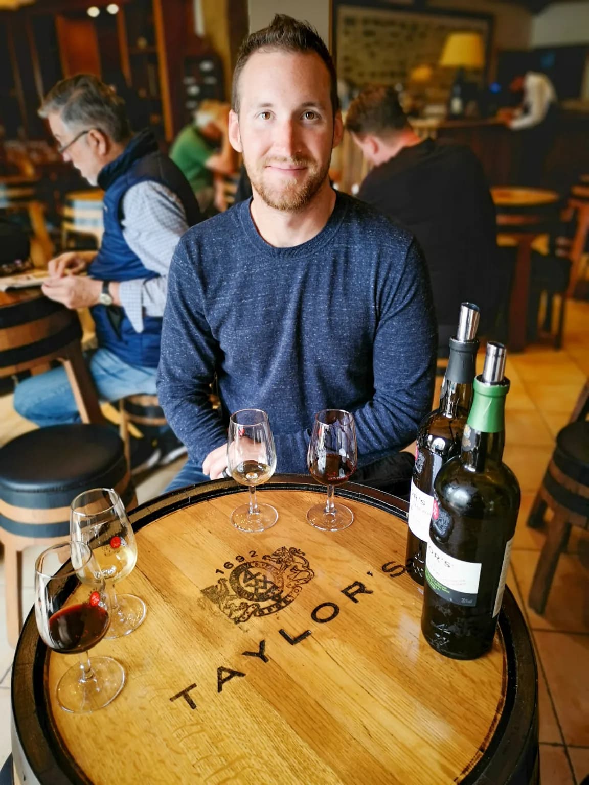 Picture of people tasting wine over a wooden barrely with a company brand.